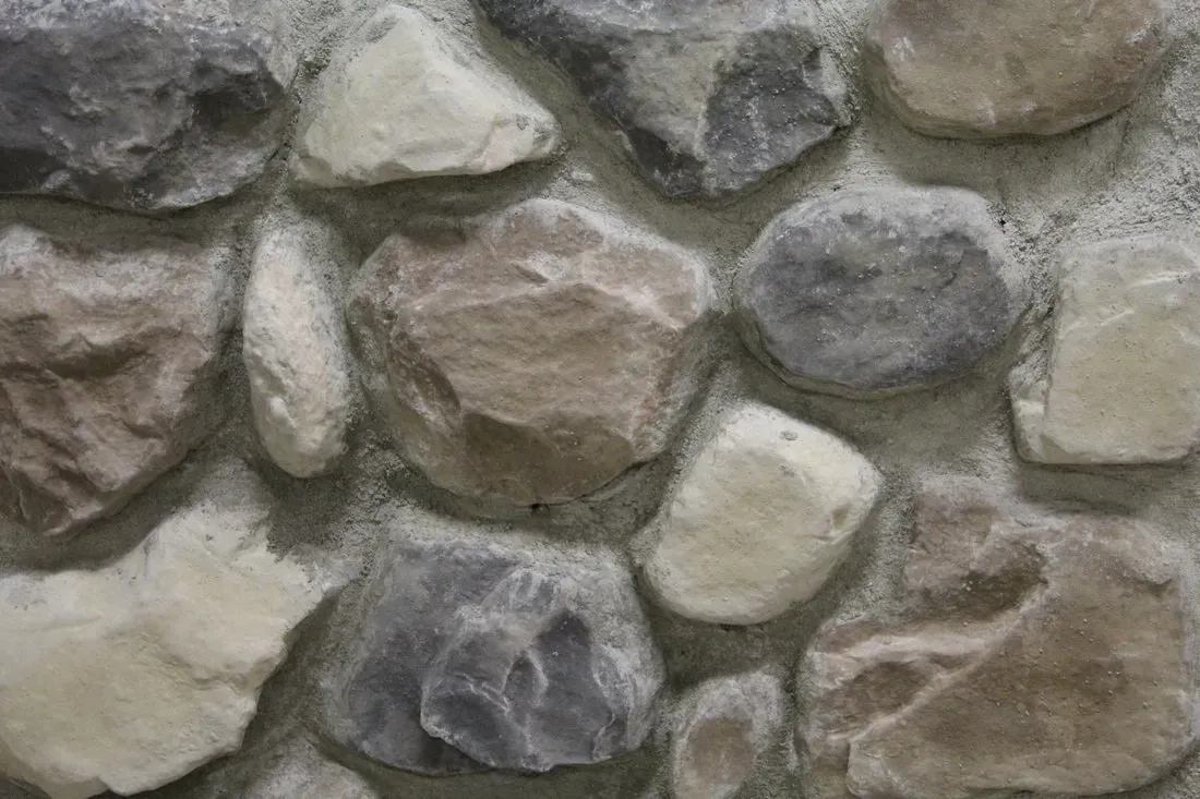 Close-up of a gray and tan stone wall with irregular rounded rocks and mortar
