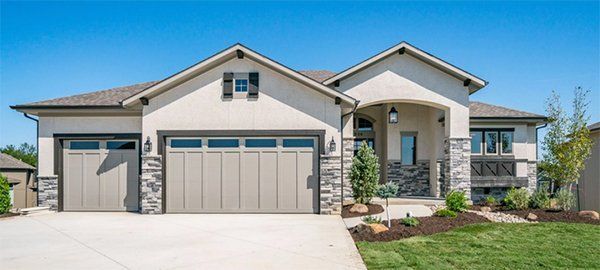 Modern suburban house with three-car garage, stone accents, and a manicured front lawn