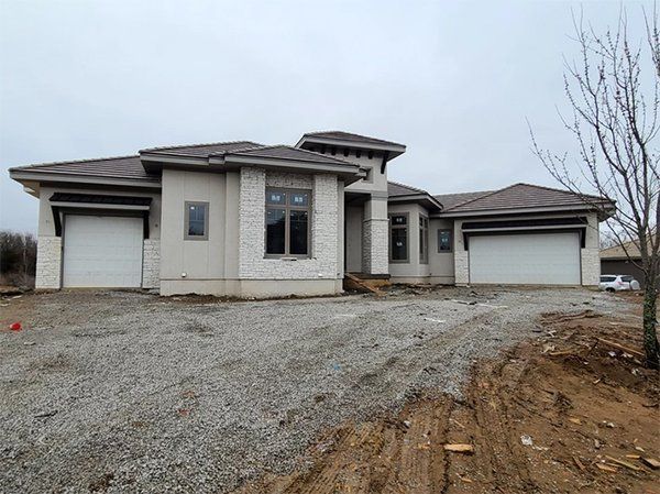 Single-story house with two garages on a gravel driveway under an overcast sky
