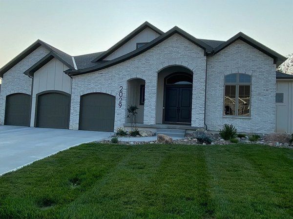 Modern gray brick house with three-car garage and green lawn at dusk
