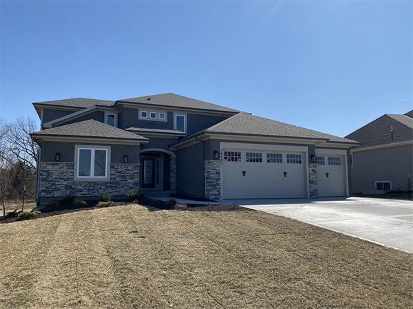 Suburban two-story house with stone exterior, front lawn, and three-car garage under a blue sky