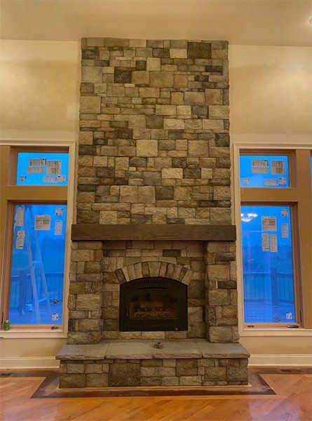 Stone fireplace centered between two windows in a warmly lit room, with a mantel and hearth.