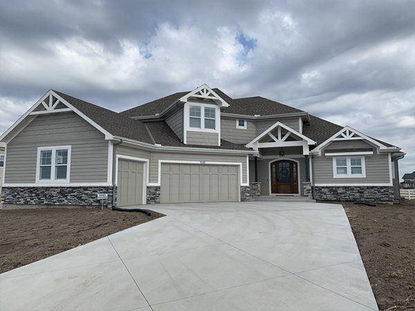 Suburban house with gray siding, white trim, two-car garage, and a wide concrete driveway under cloudy skies