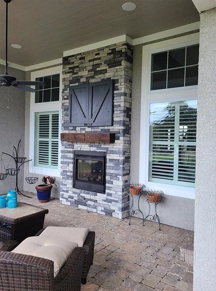 Covered patio with stone fireplace, wicker seating, and potted plants