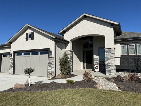 Modern suburban house with a beige exterior, gray garage, and front walkway under a clear blue sky