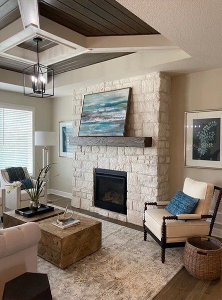 Cozy living room with white stone fireplace, blue artwork, tan chairs, and a wood coffee table