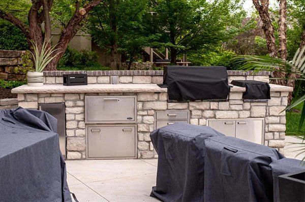 Outdoor patio with several covered grills and a stone outdoor kitchen area surrounded by trees