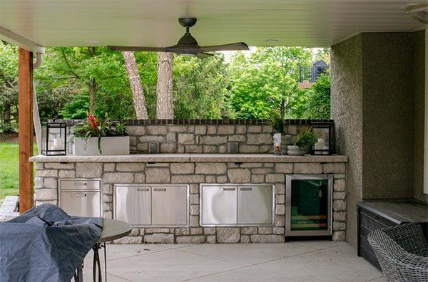 Covered outdoor patio with stone bar, built-in grill, ceiling fan, and potted plants