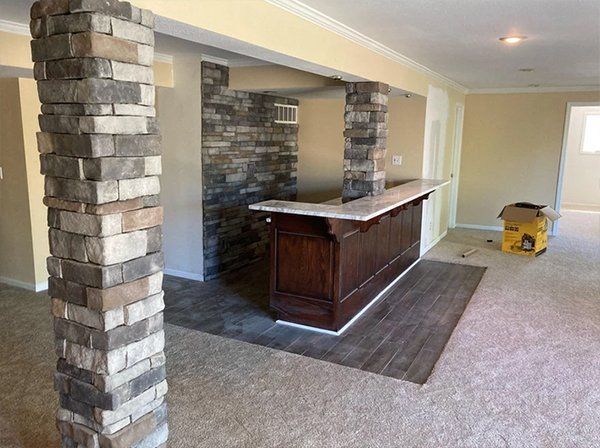 Partially finished basement bar with stone columns, wood counter, and carpeted floor