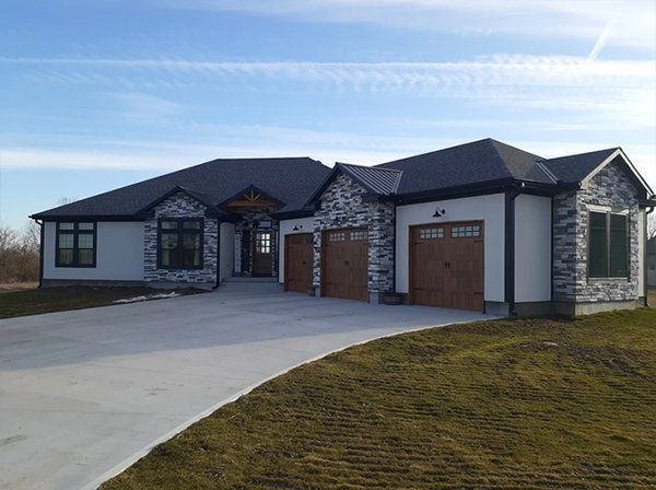 Modern single-story house with stone accents and three-car garage on a sloped driveway