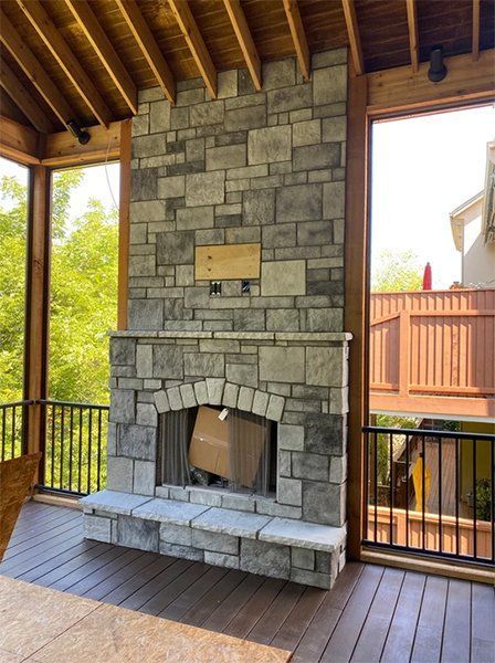 Covered patio with a stone fireplace, wooden ceiling, and open railings overlooking a yard
