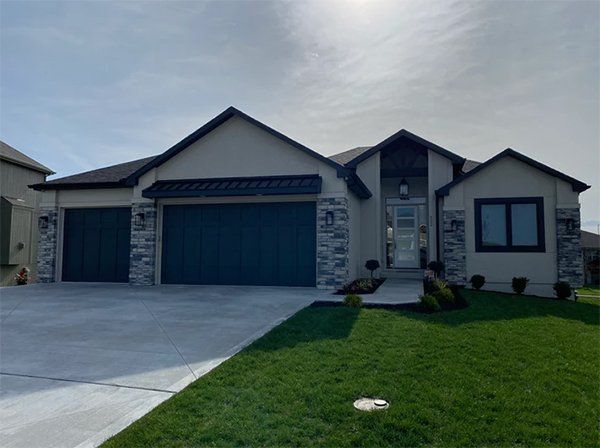 Modern single-story house with blue garage doors, stone accents, and a green lawn
