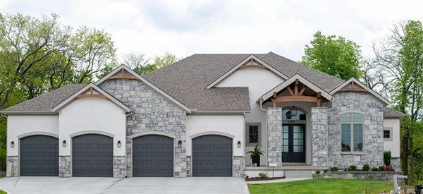 Large modern suburban house with gray stone exterior, three garage doors, and manicured lawn
