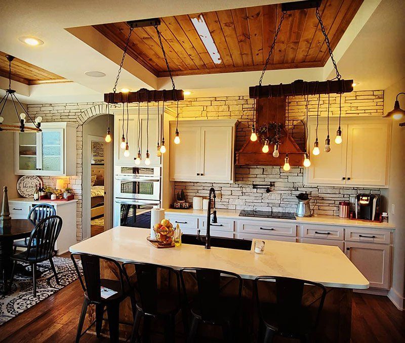 Warm farmhouse kitchen with white cabinets, wood ceiling, large island, and hanging pendant lights