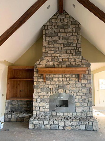 Stone fireplace with mantel and built-in shelving in a room with a vaulted ceiling.