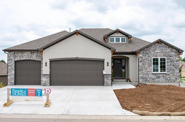 Modern single-story house with stone facade, gray garage door, and a new-build sign in front