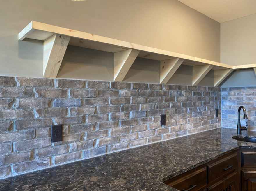 Kitchen backsplash with gray stone tile, dark granite countertop, and white shelf brackets above the counter