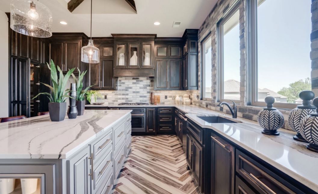 Bright modern kitchen with dark cabinets, marble countertops, pendant lights, and large windows overlooking water