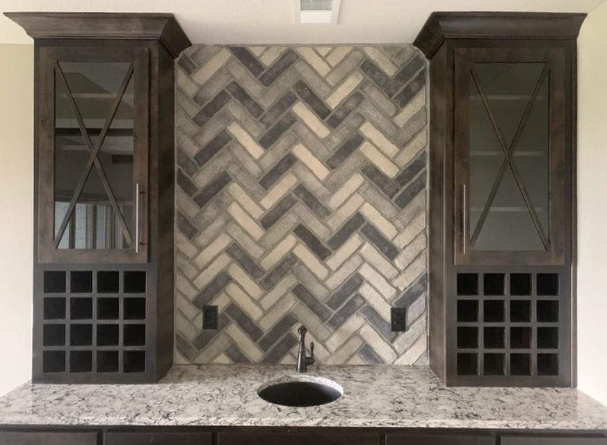 Modern kitchen sink with herringbone tile backsplash and dark cabinets on either side