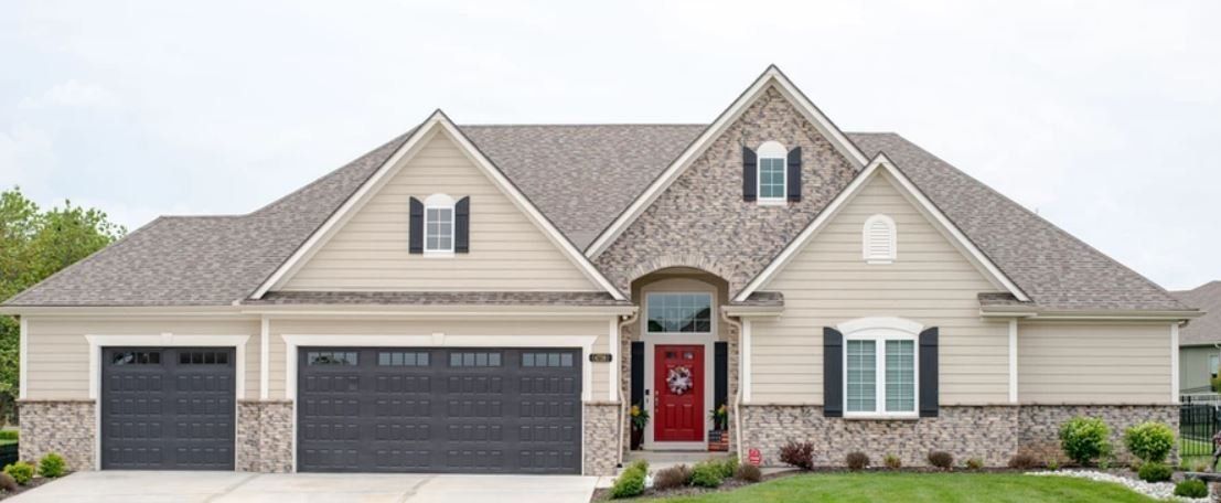 Suburban house with gray roof, white siding, three-car garage, and red front door
