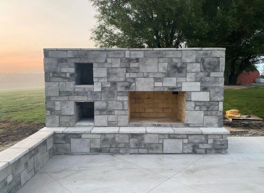 Stone outdoor fireplace built into a patio wall at sunset