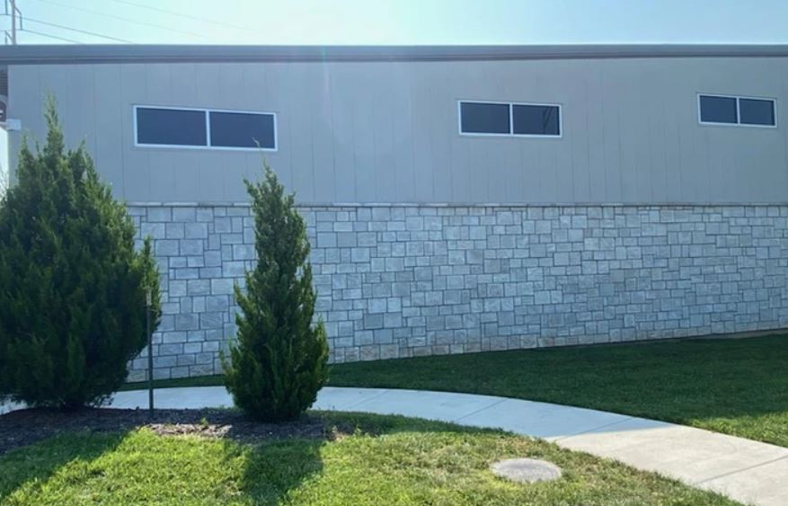 Modern house exterior with stone wall, small windows, lawn, trees, and curved walkway