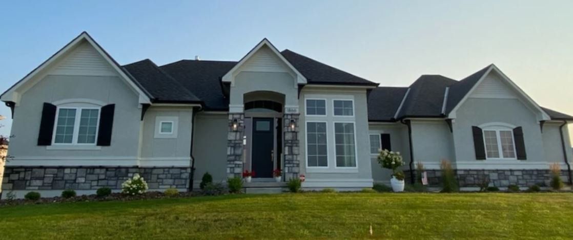 Single-story gray house with white trim, front porch, and manicured lawn under a cloudy sky