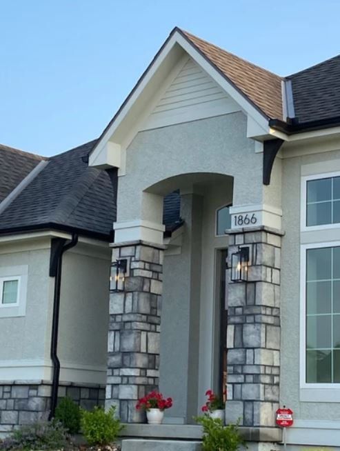 Front entrance of a gray stone house with white trim, a peaked porch, and flower pots by the door