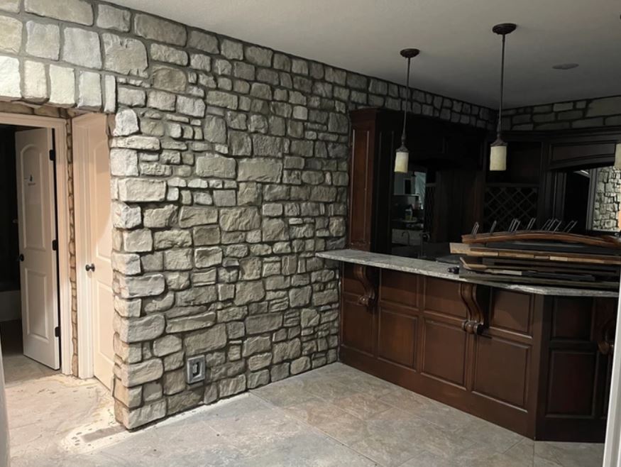 Stone-walled kitchen interior with dark wood cabinets, granite island, and pendant lights.