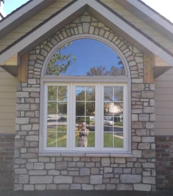 Front of a house with a stone facade, arched window, and gabled roof detail