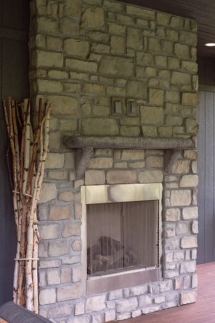 Stone fireplace with a rectangular firebox, set against a green wall and beside a bundle of tall sticks