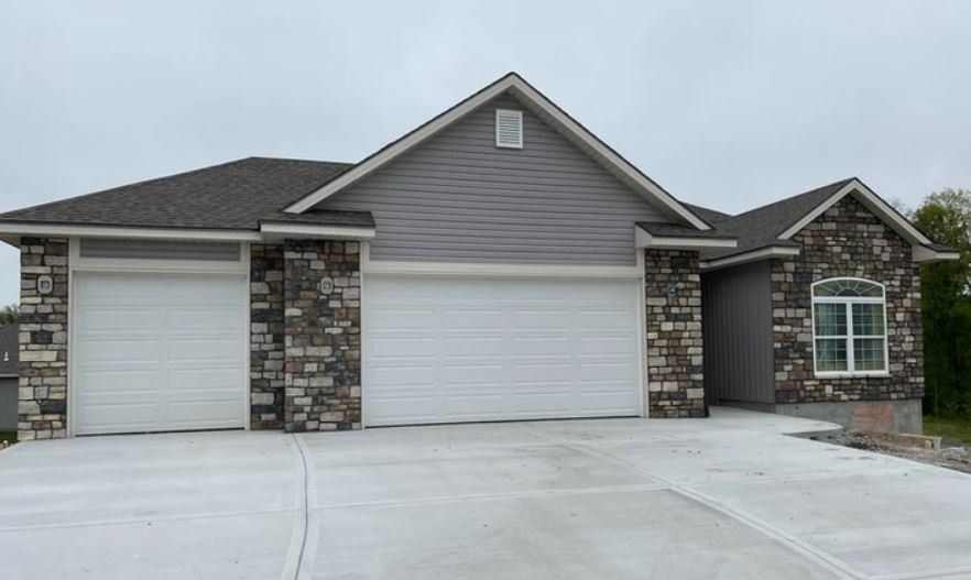 Single-story gray house with stone accents, three garage doors, and a wide concrete driveway