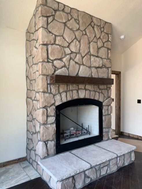 Stone fireplace with dark mantel and black firebox in a beige room, with tiled hearth bench.