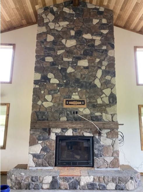 Stone fireplace with a black insert and wood mantel in a vaulted room with two small windows.