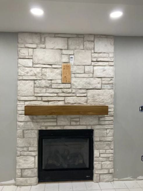 Stone fireplace with wooden mantel and black insert against a gray wall