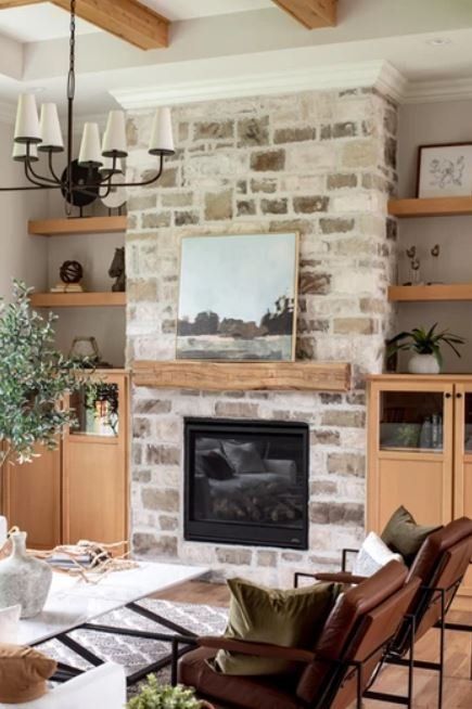 Stone fireplace with black insert in a cozy living room, framed by wood shelves, decor, and exposed beams