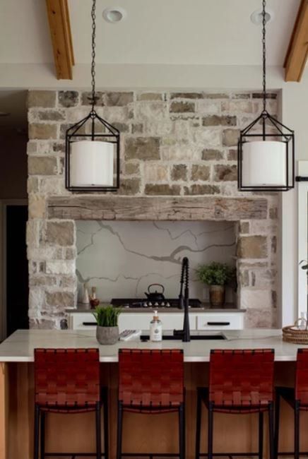Modern kitchen with stone backsplash, white island, black faucet, and three red bar stools beneath pendant lights