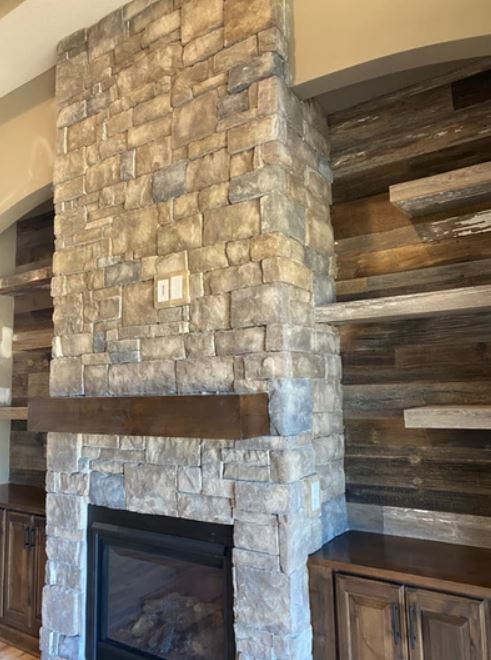 Stone fireplace with wood mantel and stacked wood accent wall in a living room