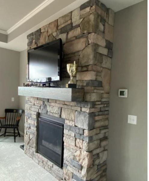 Living room stone fireplace with mounted TV and white mantel, beside a gray wall and light carpet