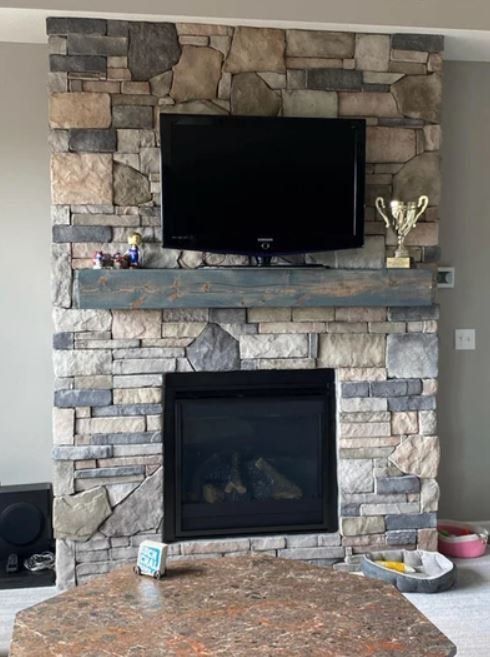 Stone fireplace wall with mounted TV and a glass-front fireplace beneath a mantel.