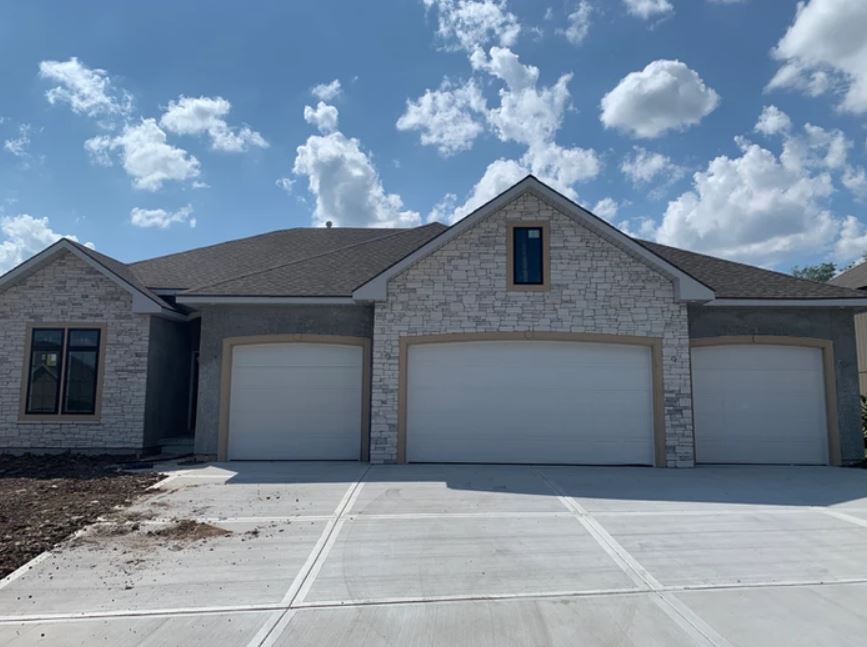 Three-car suburban garage with stone facade and gray roof under a blue sky with clouds