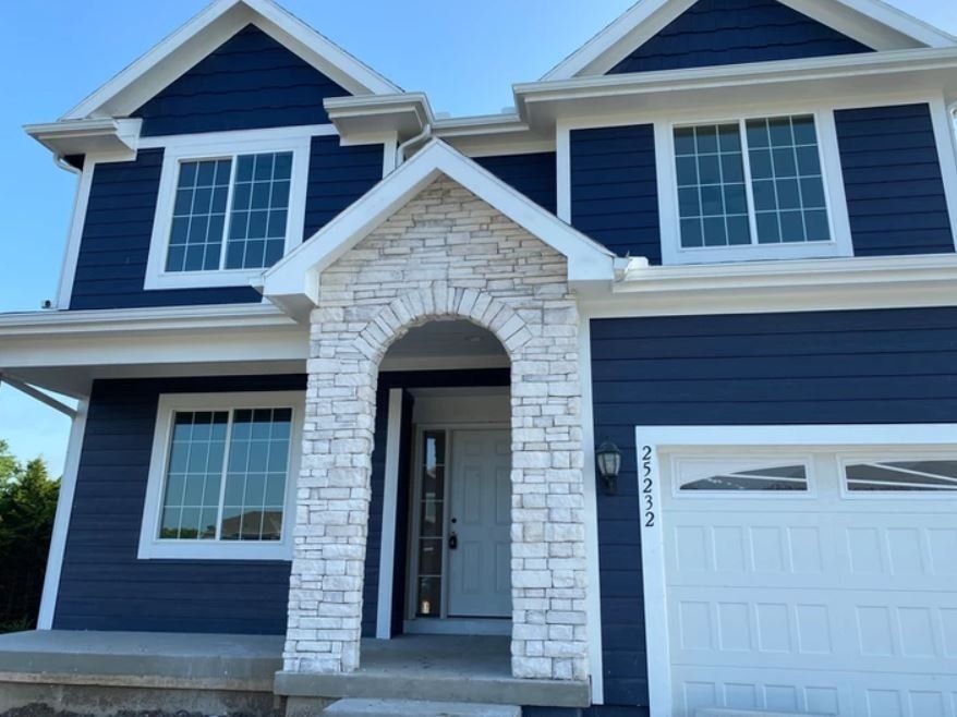 Two-story blue house with stone entry arch and white garage door