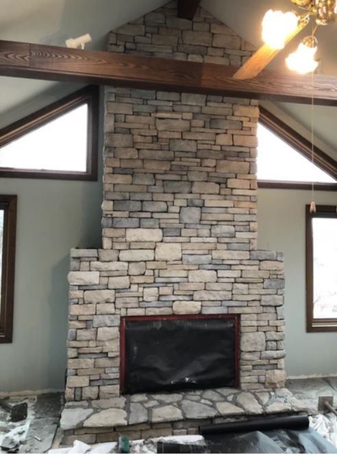 Stone fireplace with a red-trimmed black firebox in a vaulted room with exposed beams and windows