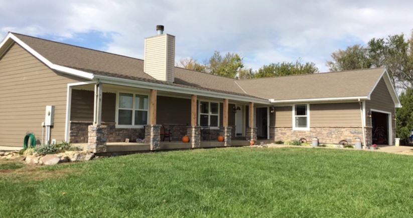 Single-story beige house with a front porch, stone accents, and a large green lawn