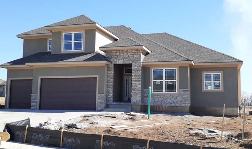 Modern beige two-story house with stone accents, three-car garage, and unfinished front yard