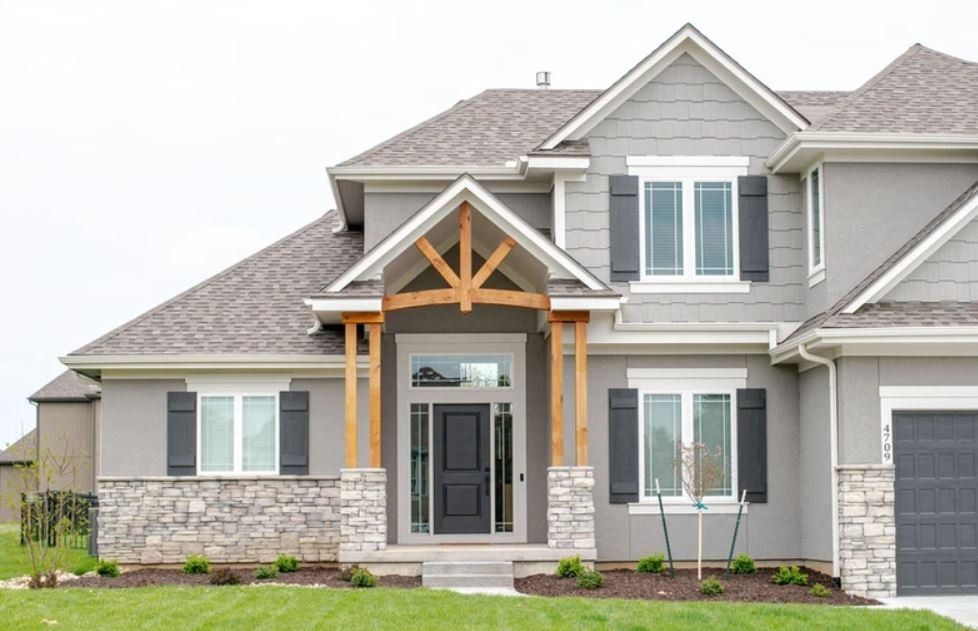 Front view of a gray suburban house with stone accents, gabled roof, and covered entry porch