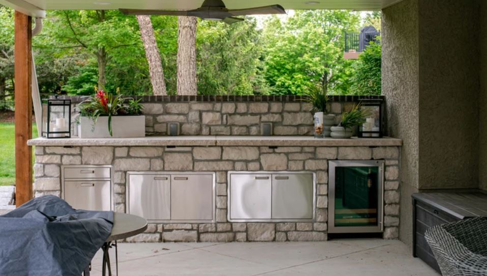 Outdoor stone backyard kitchen with grill, cabinets, and covered patio seating area