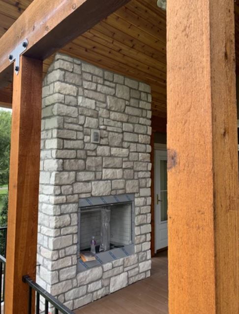 Stone fireplace with a recessed firebox under a wooden porch ceiling.