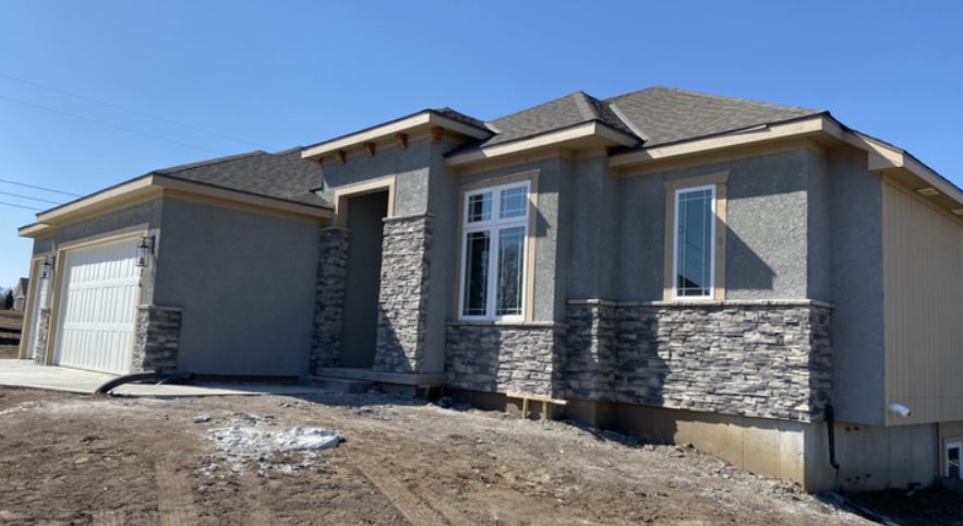 New gray house exterior with stone accents, garage, and unfinished front yard under a clear blue sky