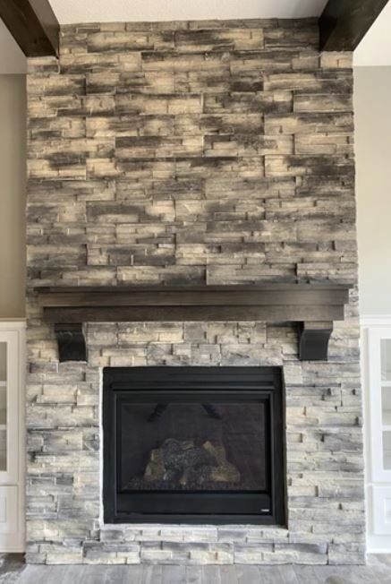 Stone fireplace with a dark wood mantel and black insert in a living room.